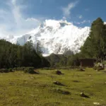 Nanga Parbat north face rising above the meadow and a wooden cottage at Fairy Meadows