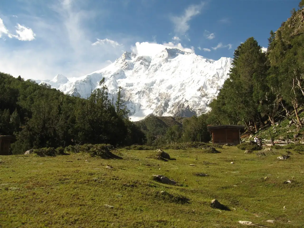 Nanga Parbat north face rising above the meadow and a wooden cottage at Fairy Meadows
