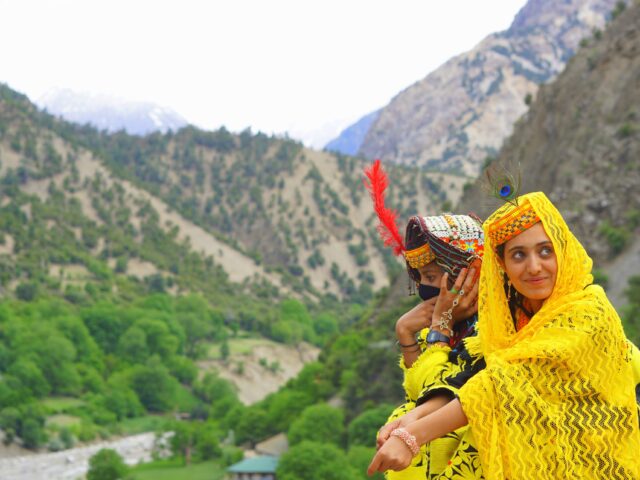 Two Kalasha girls in traditional dress overlooking Bumburet village during the Chilam Joshi festival
